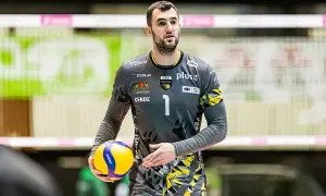 Bartłomiej Lipiński, siatkarz w szarym stroju z numerem 1, trzyma piłkę do siatkówki.