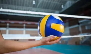 Piłka do siatkówki w dłoni, gotowa do zagrania nad siatką w hali sportowej.