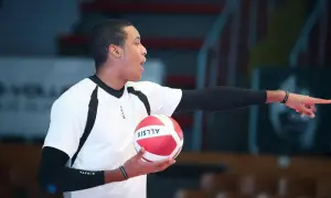 Młody siatkarz z piłką w dłoni, wskazujący palcem, jakby tłumaczył zasady gry, która narodziła się z potrzeby aktywnego spędzania czasu.