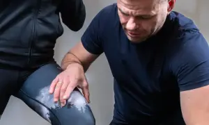 Fizjoterapeuta sprawdza kolano biegacza podczas ćwiczeń rehabilitacyjnych.