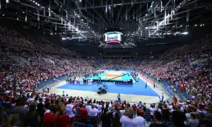 Trybuna kibiców w biało-czerwonych barwach dopingująca zawodników podczas meczu siatkówki. W tle boisko i zawodnicy.