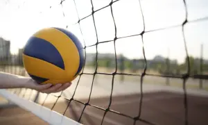 Piłka do siatkówki w dłoni, tuż przed siatką. Może to być początek akcji lub błąd ustawienia w siatkówce.