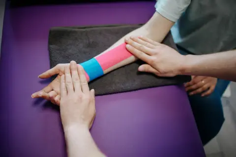 Fizjoterapeuta aplikuje tejpy na palce i nadgarstek pacjenta, by zapewnić wsparcie i ulgę.
