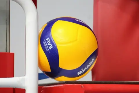Żółta piłka do siatkówki Mikasa z niebieskimi pasami, z logo FIVB Approved.