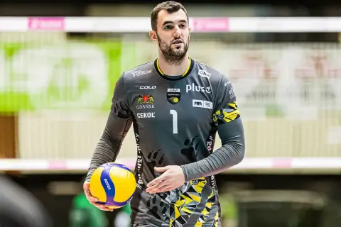 Bartłomiej Lipiński, siatkarz w szarym stroju z numerem 1, trzyma piłkę do siatkówki.