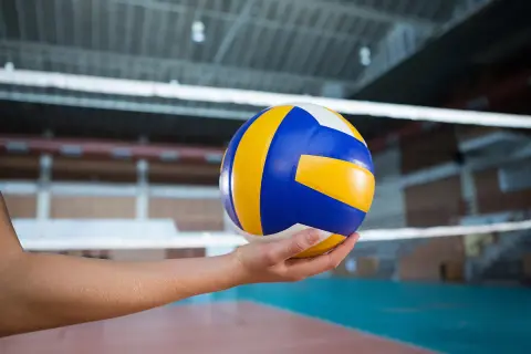 Piłka do siatkówki w dłoni, gotowa do zagrania nad siatką w hali sportowej.