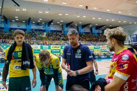 Trener Ireneusz Mazur udziela wskazówek siatkarzom w hali sportowej, wśród kibiców.