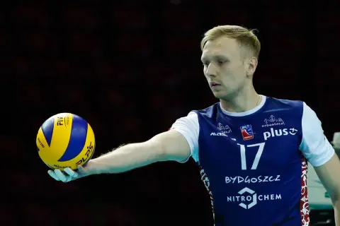 Siatkarz Mateusz Sacharewicz z piłką w dłoni, gotowy do zagrywki.