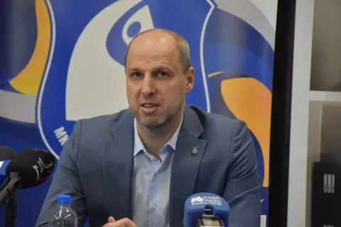 Dominik Kwapisiewicz w garniturze przed mikrofonami, na tle niebiesko-żółtego logo.