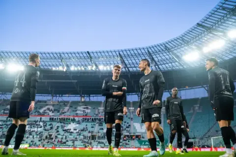 Piłkarze w czarnych strojach stoją na boisku. Jeden z nich ma opaskę w barwach narodowych. Czy to oznacza, że przegrali mecz i dostali walkower? Co to znaczy?