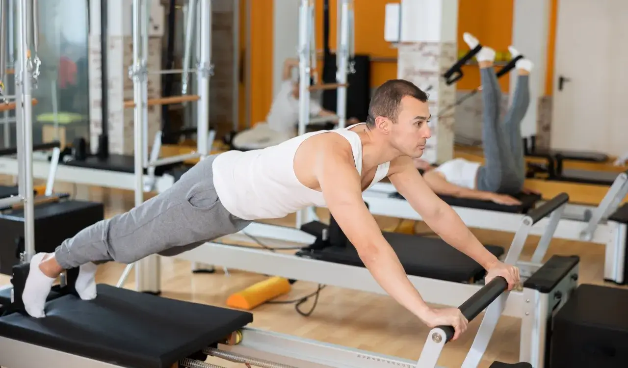 Mężczyzna i kobieta ćwiczą na reformerach. Pilates co daje? Wzmocnienie mięśni, poprawa postawy i elastyczności.
