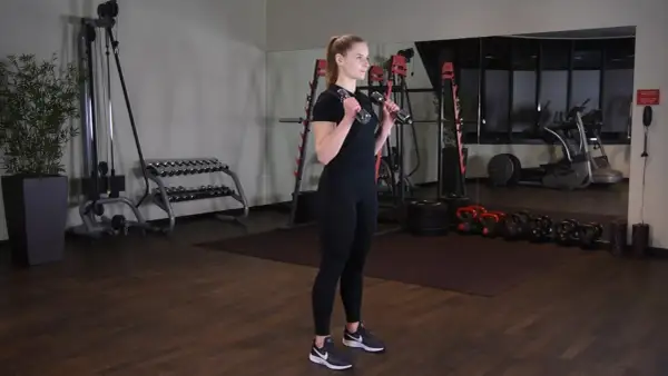 Kobieta wykonuje uginanie ramion z hantlami, ćwicząc bicepsy w siłowni.